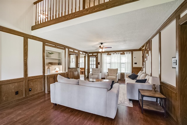 living room featuring wainscoting, a decorative wall, a ceiling fan, and dark wood-type flooring