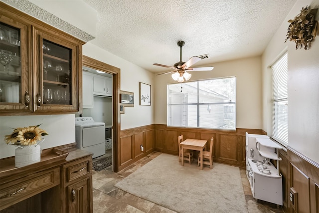 dining room featuring ceiling fan, washer / dryer, a wainscoted wall, and a textured ceiling