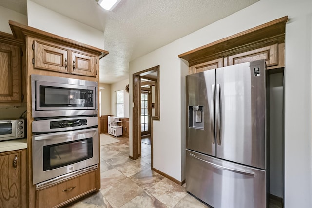 kitchen featuring a toaster, a textured ceiling, baseboards, brown cabinetry, and appliances with stainless steel finishes