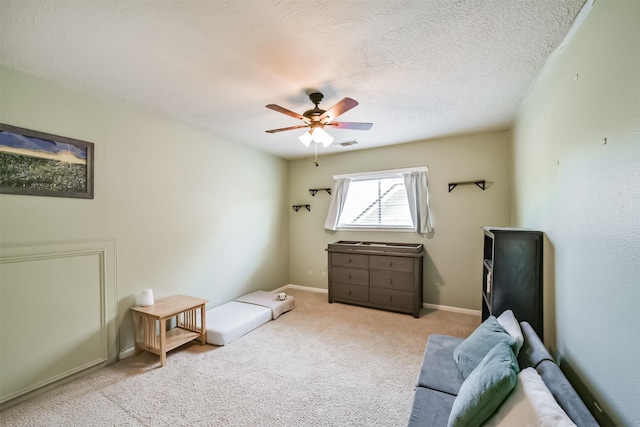 living area with a textured ceiling, baseboards, visible vents, carpet, and ceiling fan