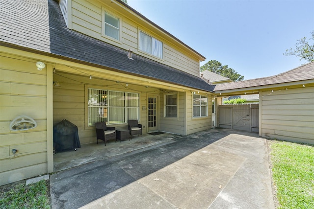 back of property with a gate, roof with shingles, and a patio