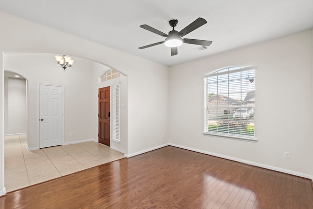 empty room featuring wood-type flooring, arched walkways, visible vents, and baseboards