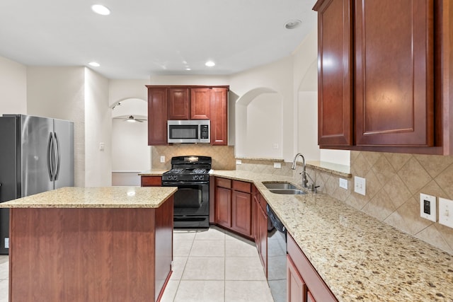 kitchen with backsplash, a sink, light stone countertops, a center island, and black appliances