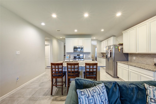 kitchen with a kitchen island with sink, open floor plan, light tile patterned flooring, and appliances with stainless steel finishes