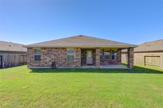 rear view of property with brick siding, a fenced backyard, a lawn, and a patio area