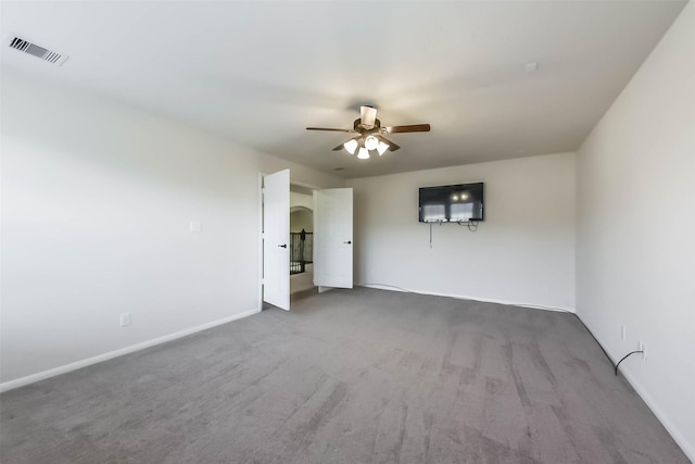 carpeted spare room with visible vents, arched walkways, baseboards, and ceiling fan