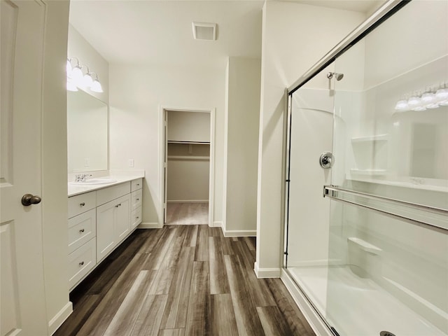 bathroom featuring a shower stall, vanity, a spacious closet, visible vents, and wood finished floors