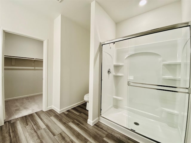 bathroom with toilet, a shower stall, wood finished floors, and baseboards