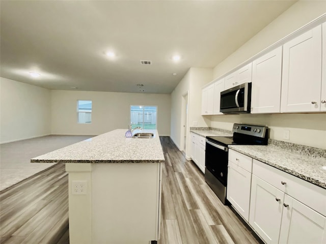 kitchen featuring an island with sink, white cabinets, light wood-style floors, stainless steel appliances, and a sink