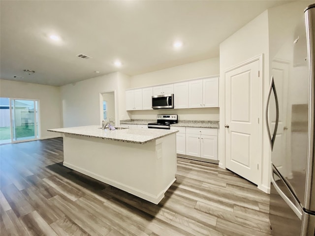 kitchen with appliances with stainless steel finishes, white cabinetry, light wood finished floors, a center island with sink, and light stone counters
