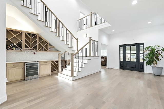 foyer with a towering ceiling, a bar, stairs, wine cooler, and light wood finished floors