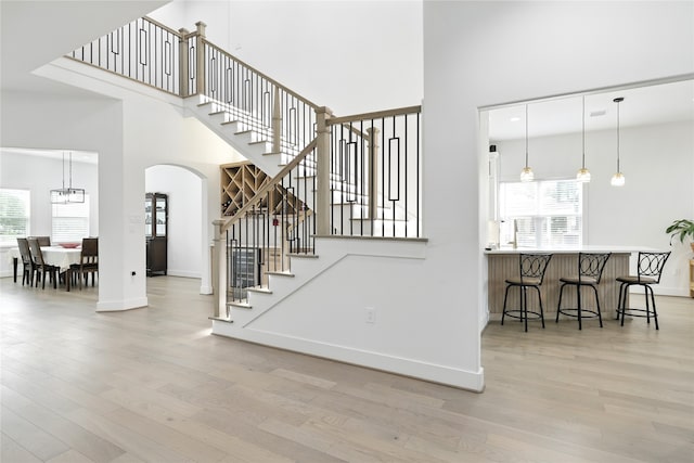 staircase with baseboards, arched walkways, a notable chandelier, a high ceiling, and wood finished floors