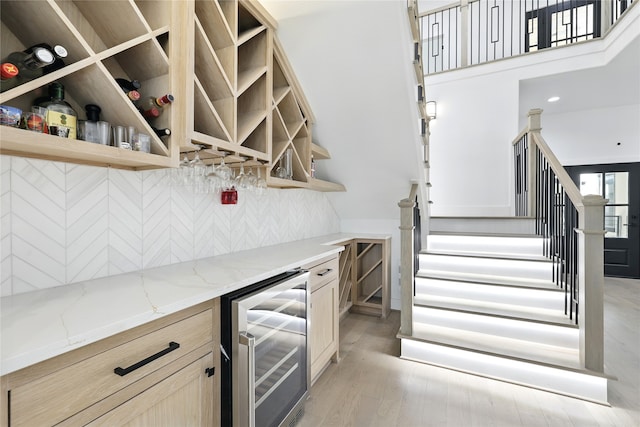 bar featuring a bar, wine cooler, stairway, light wood finished floors, and decorative backsplash