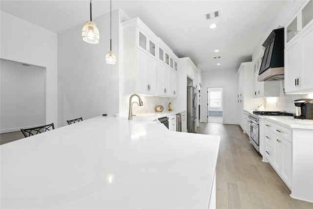kitchen featuring custom exhaust hood, a peninsula, visible vents, appliances with stainless steel finishes, and a sink