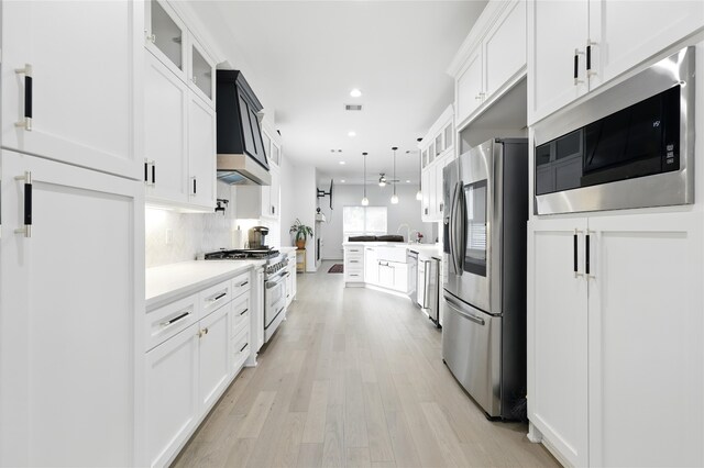 kitchen with glass insert cabinets, decorative backsplash, a peninsula, stainless steel appliances, and light wood finished floors