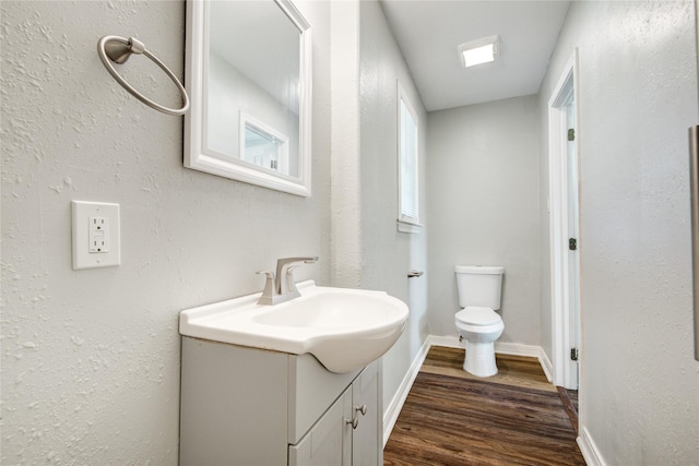 half bathroom featuring toilet, wood finished floors, vanity, and baseboards