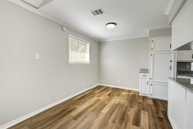 unfurnished dining area featuring dark wood finished floors, baseboards, ornamental molding, and visible vents