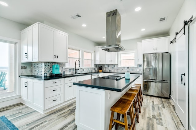 kitchen featuring visible vents, stainless steel refrigerator with ice dispenser, a barn door, a sink, and island exhaust hood
