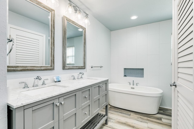 full bathroom with wood finished floors, double vanity, a sink, and a freestanding tub