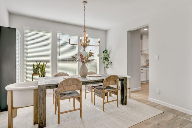 dining area featuring baseboards, light wood-type flooring, and an inviting chandelier
