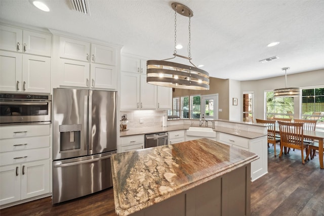 14832 Oak Shores Dr, Willis, TX 77318 - kitchen featuring appliances with stainless steel finishes, a sink, a peninsula, a textured ceiling, and white cabinetry