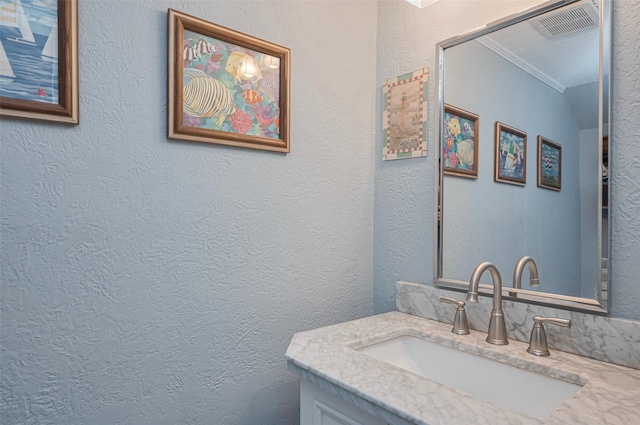bathroom featuring crown molding, visible vents, vanity, and a textured wall