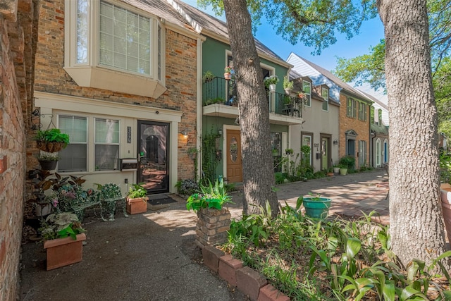 view of front of home featuring a balcony, stucco siding, and brick siding