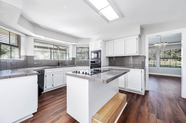 kitchen with an inviting chandelier, a sink, black appliances, dark wood-type flooring, and a kitchen island