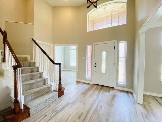 foyer entrance with stairway, light wood-style floors, a high ceiling, and baseboards