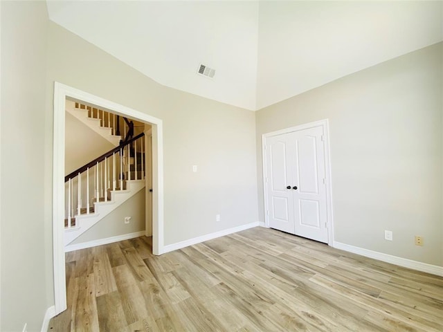 unfurnished room featuring visible vents, baseboards, light wood-type flooring, stairway, and high vaulted ceiling