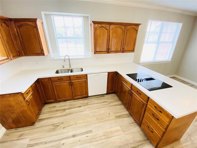kitchen featuring dishwasher, a sink, a peninsula, brown cabinets, and black electric stovetop