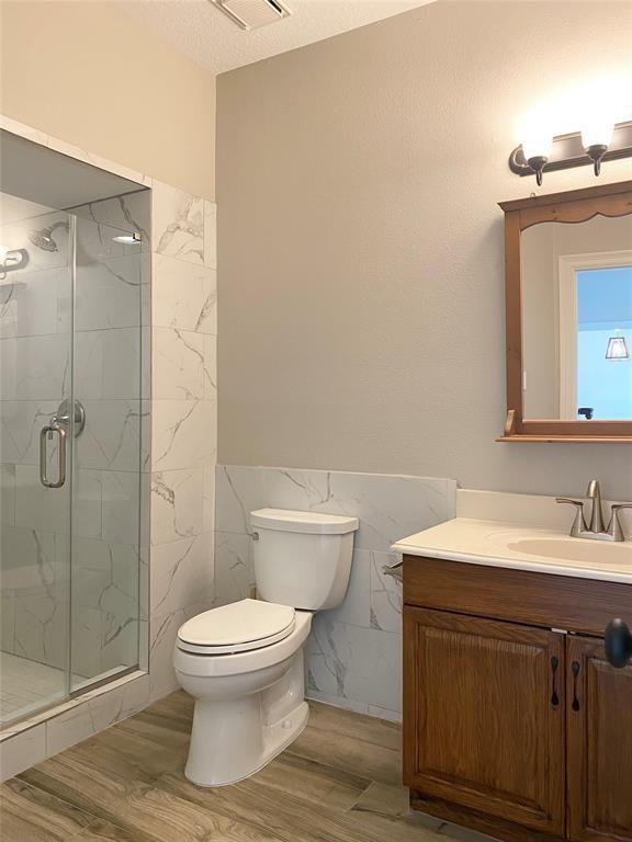 full bath featuring vanity, toilet, wood finished floors, tile walls, and a marble finish shower