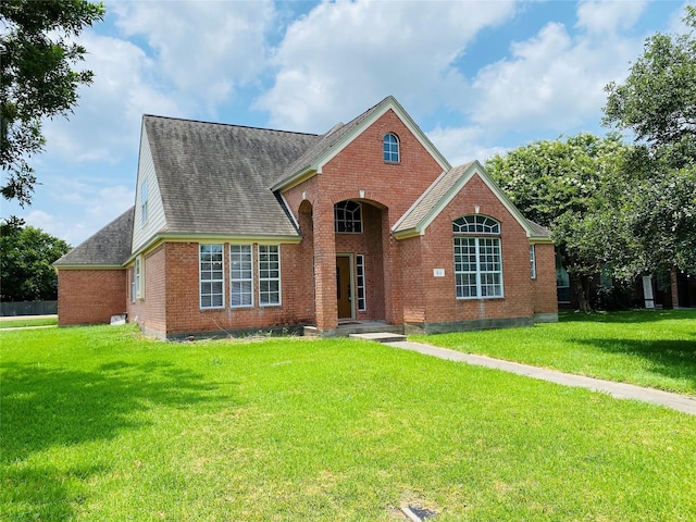 view of front of home with brick siding, a front yard, and roof with shingles