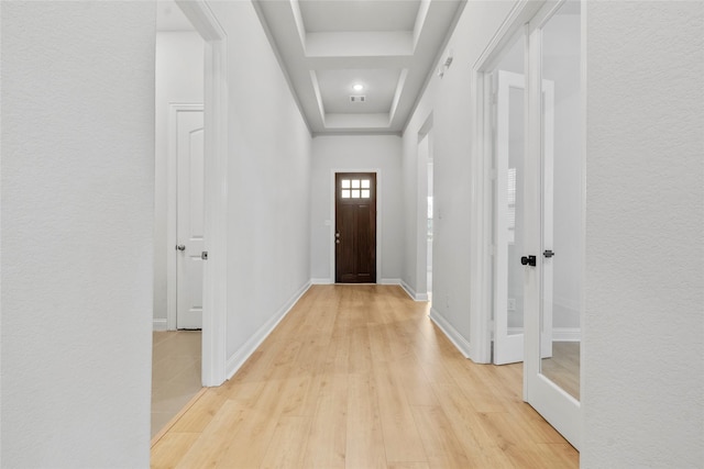 doorway featuring a tray ceiling, light wood-style floors, and baseboards