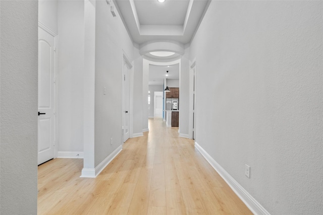 hall featuring a raised ceiling, light wood finished floors, and baseboards