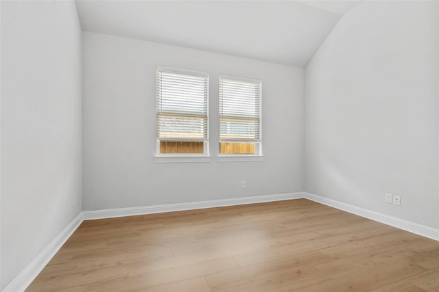 spare room featuring baseboards, light wood-type flooring, and vaulted ceiling