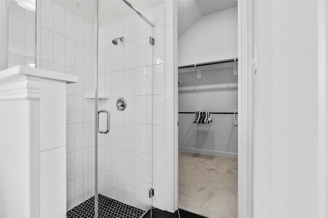 bathroom with a walk in closet, a stall shower, and vaulted ceiling