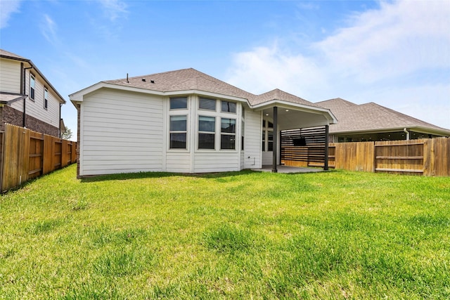rear view of property with roof with shingles, a yard, a fenced backyard, and a patio area
