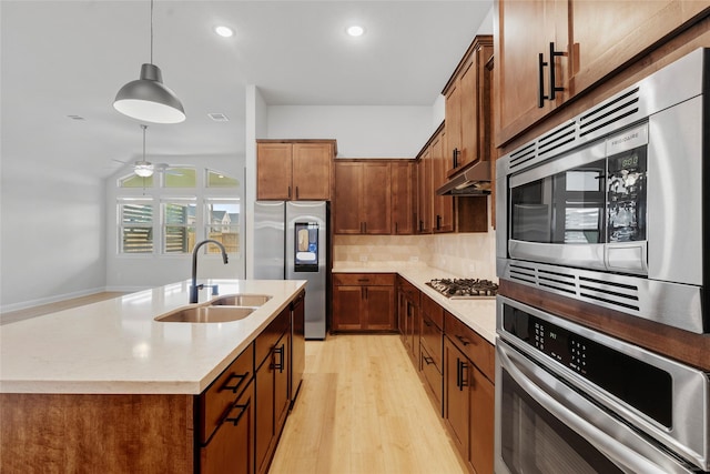 kitchen with decorative light fixtures, a sink, under cabinet range hood, light wood finished floors, and stainless steel appliances