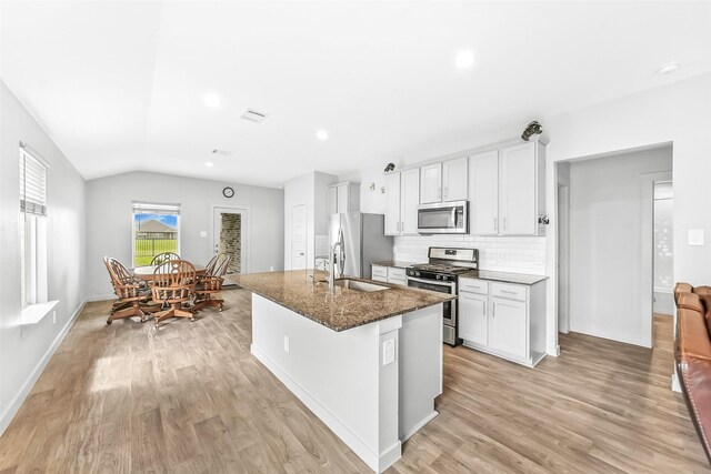 kitchen with appliances with stainless steel finishes, a sink, light wood-style flooring, tasteful backsplash, and a center island with sink