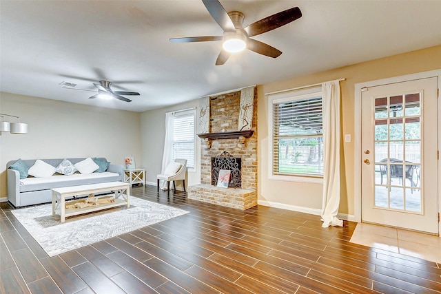 living area featuring dark wood-style flooring, baseboards, a brick fireplace, visible vents, and ceiling fan