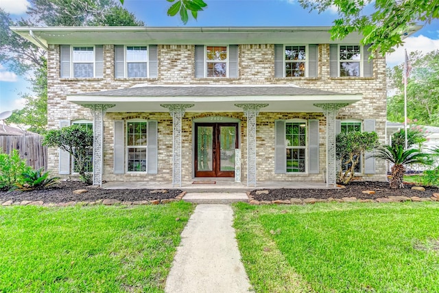 view of front of property featuring a porch, fence, a front lawn, brick siding, and french doors