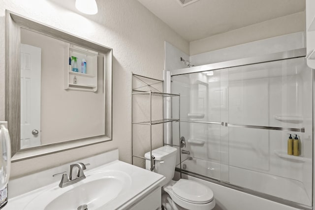 full bath featuring toilet, vanity, a textured wall, and bath / shower combo with glass door
