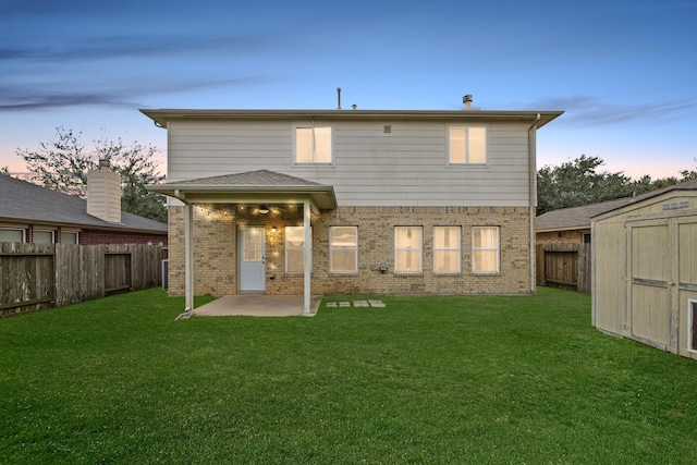 rear view of house with a patio, a shed, a fenced backyard, an outbuilding, and a lawn