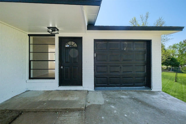 property entrance featuring an attached garage, driveway, and brick siding