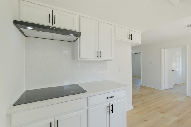 kitchen with baseboards, white cabinets, light wood-style floors, under cabinet range hood, and black electric stovetop
