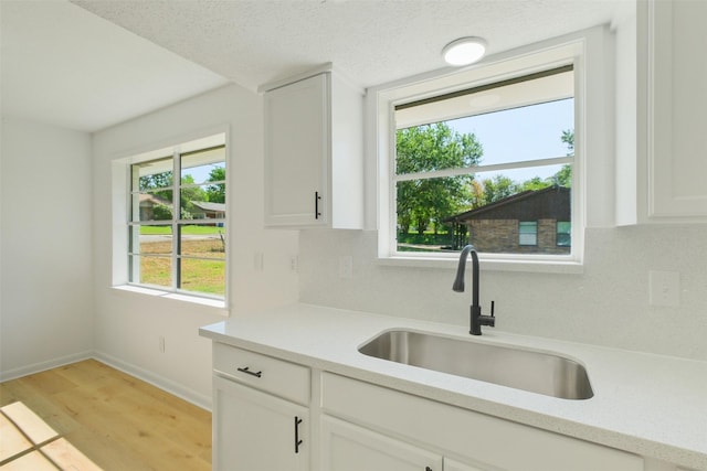 kitchen with light countertops, light wood finished floors, a sink, and white cabinets