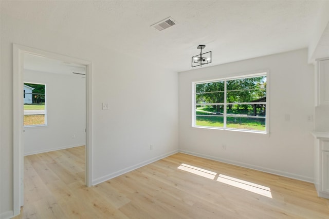 empty room with visible vents, baseboards, light wood finished floors, and a notable chandelier