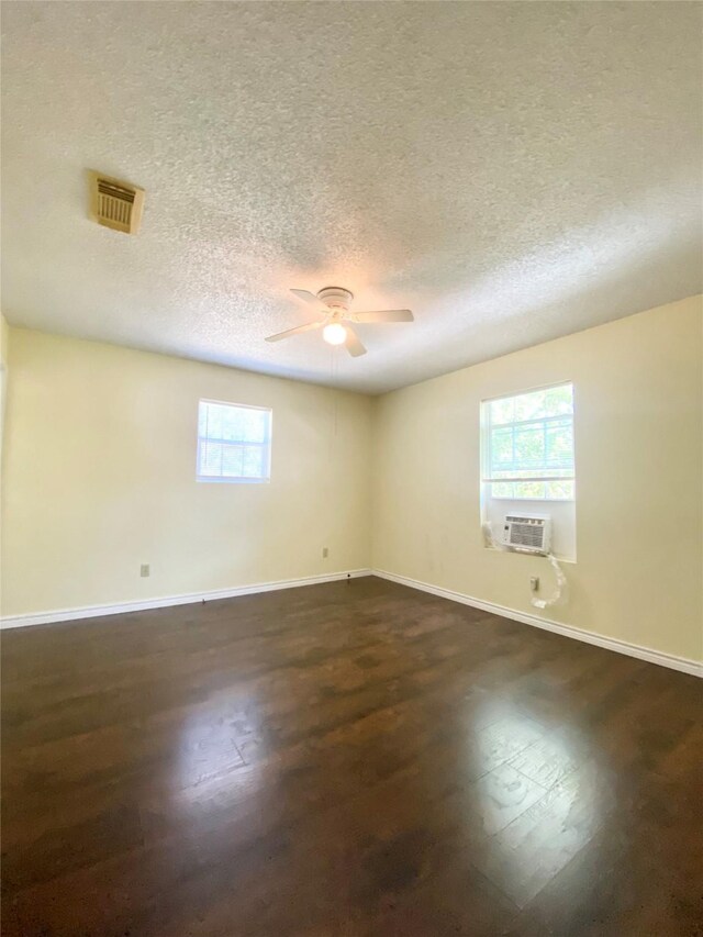 empty room with dark wood-style flooring, ceiling fan, a textured ceiling, baseboards, and visible vents