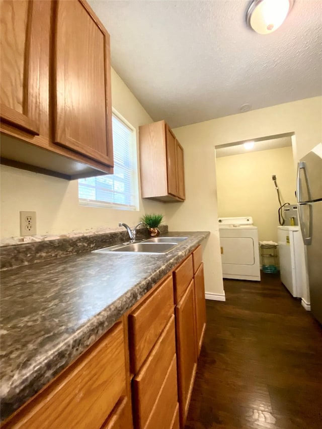kitchen with dark wood-style flooring, dark countertops, a sink, separate washer and dryer, and freestanding refrigerator